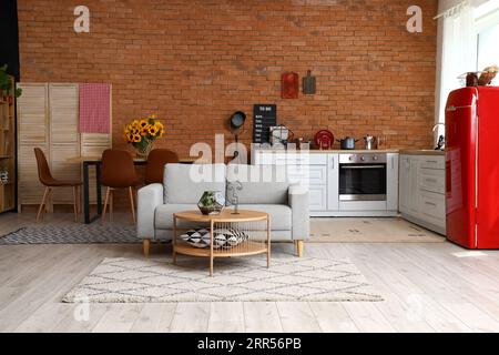 Inneneinrichtung der modernen offenen Küche mit grauem Sofa, Couchtisch und weißen Ablagen Stockfoto