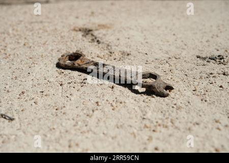 Ein rostiger alter Schraubenschlüssel liegt auf dem sandigen Boden Stockfoto