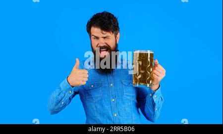 Bierverkostung. Bärtiger Mann trinkt Bier aus einem Becher in Bar oder Pub. Gutaussehender Mann mit einem Pint Lagerbier mit einem OK-Zeichen, Daumen hoch. Mann, der zuzwinkert Stockfoto