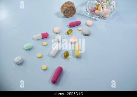 Viele Pillen verstreut auf der Oberfläche oder von der Flasche in Frau Hand Palm.Vitamine Medikament Antibiotika Tabletten verschiedene Form Kapseln.isolierte graue Fliesen Imita Stockfoto