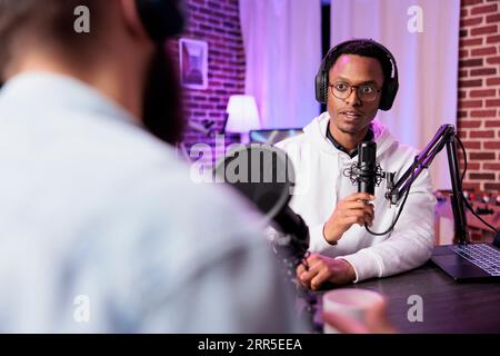 Podcast-Moderator, der Live-Gespräche mit man führt und es online streamt, damit das Publikum die Show sehen kann. Influencer, der mit Gästen chattet und im Wohnzimmer des Heimstudios mit rgb-Leuchten sendet Stockfoto