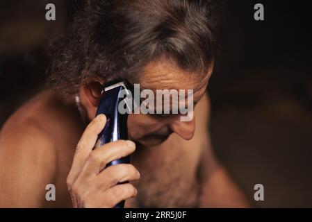 Ein älterer Mann, etwa 60 Jahre alt, serbischer Nationalität, schneidet sich mit einem Haarschneider seine eigenen Haare. Stockfoto