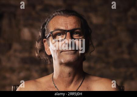 Ein älterer Mann, etwa 60 Jahre alt, serbischer Nationalität mit langen Haaren, die eine Brille vor einem dunklen Hintergrund tragen, schaut auf die Kamera. Künstler, kreativ Stockfoto