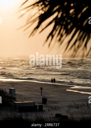 Ein Paar Silhouetten, die bei Sonnenaufgang an einem verlassenen oder leeren Strand entlang laufen, während die Wellen des Golfs von Mexiko in Destin Florida, USA, in ihre Füße treten. Stockfoto