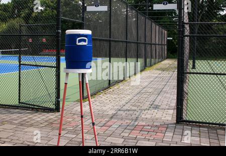 Blauer Wasserkrug auf einem Stativständer neben den Tennis- und Pickleball-Plätzen, umgeben von schwarzen Zäunen. Stockfoto