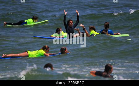 Gilgo Beach, New York, USA - 25. Juli 2023: Kinder in neongrünen Hemden reiten auf Wellen beim Surfen im Bunger Surf Camp mit ihrem Ratgeber in der Mitte Stockfoto