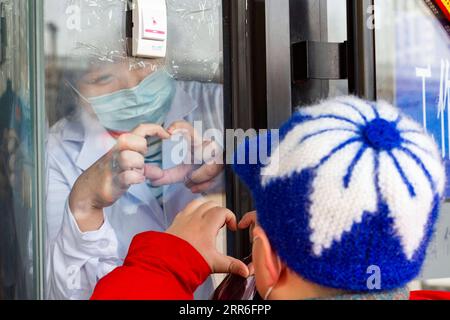 210213 -- PEKING, 13. Februar 2021 -- Zheng Yingying, ein medizinischer Arbeiter vom Volkskrankenhaus des Daowai Bezirks von Harbin, macht eine Handherzgeste zu ihrem besuchenden Sohn hinter einer Glastür in einem Quarantänezentrum in Harbin, nordöstliche Provinz Heilongjiang, 11. Februar 2021. XINHUA FOTOS DES TAGES XiexJianfei PUBLICATIONxNOTxINxCHN Stockfoto