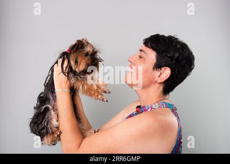 Eine Frau hält liebevoll einen schönen Yorkshire-Terrier. Isoliert auf grauem Hintergrund. Stockfoto