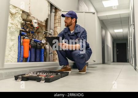 Der Klempner diagnostiziert vor der Reparatur die Rohre im Wasserversorgungssystem und macht sich Notizen in der Zwischenablage Stockfoto