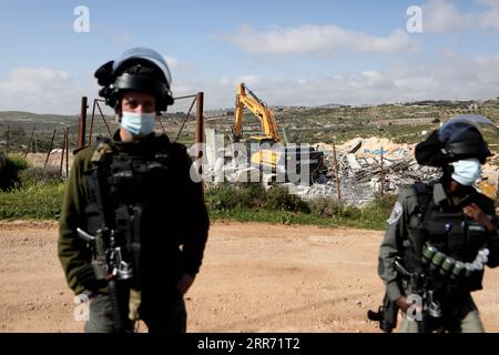 210308 -- HEBRON, 8. März 2021 -- ein israelischer Soldat und ein Mitglied der israelischen Grenzpolizei stehen als Bagger und zerstören ein palästinensisches Haus, das sich im Bau befindet, und behaupten, es sei ohne Erlaubnis gebaut worden, in der Stadt Bani Naim in der Nähe der Westbank-Stadt Hebron, 8. März 2021. Foto von /Xinhua MIDEAST-HEBRON-HAUS-ABRISS MamounxWazwaz PUBLICATIONxNOTxINxCHN Stockfoto