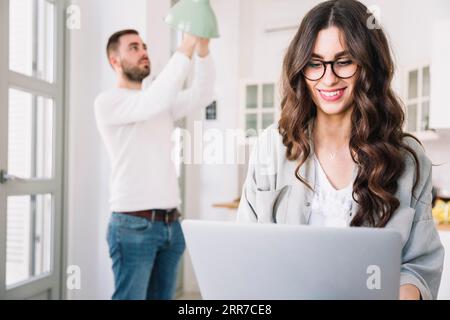 Frau Laptop, während Mann die Glühlampe wechselt Stockfoto