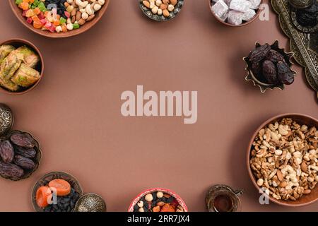 Metallische Erdschale getrocknete Früchte Datteln Lukum Nüsse Baklava angeordnet kreisförmig geformten braunen Hintergrund Stockfoto