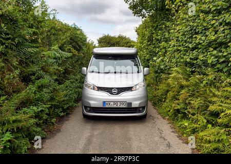 Campervan, Minicamper Nissan NV200 auf schmaler einspuriger Landstraße, hohe dichte Hecken am Straßenrand, schlechte Sicht, Cornwall, England Stockfoto