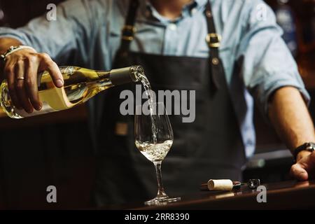 Sommeliermännchen gießt Weißwein in langstielige Weingläser. Stockfoto