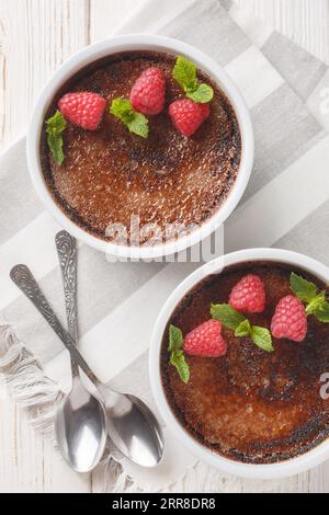 Schokoladencreme-Brulee mit Karamellkruste, garniert mit Minze und Himbeeren, auf dem Tisch in Rapinrot. Vertikale Draufsicht von oben Stockfoto