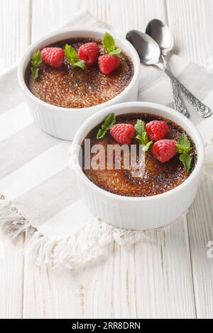 Spanisches Schokoladen-Creme-Brulee mit karamellisiertem Zucker auf der Oberseite, verziert mit Minze und Himbeeren in einem Ramekin auf dem Tisch. Vertikal Stockfoto