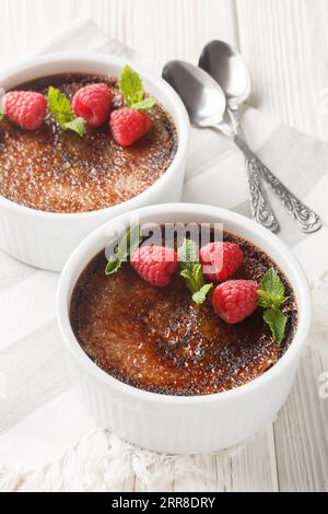 Schokoladencreme-Brulee mit Karamellkruste, garniert mit Minze und Himbeeren, auf dem Tisch in Rapinrot. Vertikal Stockfoto