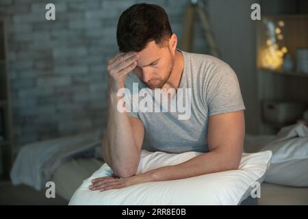 asiatischer Mann, der an Schlaflosigkeit leidet und auf dem Bett sitzt Stockfoto