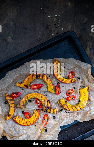 Ein gegrillter Hokkaido-Kürbis auf einem Backblech mit Backpapier aus biologischem Anbau mit Chilischoten Stockfoto