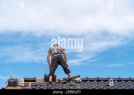 Arbeiter auf dem Dach eines Einfamilienhauses, der eine Dachabdeckung aus Keramikfliesen baut Stockfoto