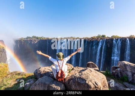 Frau sitzt auf einem Felsen und genießt die Victoria Falls - Simbabwe Stockfoto
