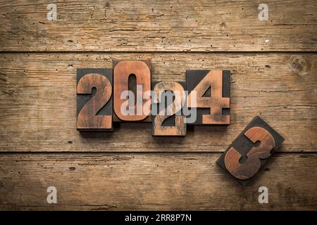 Änderung von Jahr 2023 auf 2024 geschrieben mit Vintage-Buchdruckblöcken auf rustikalem Holzhintergrund Stockfoto