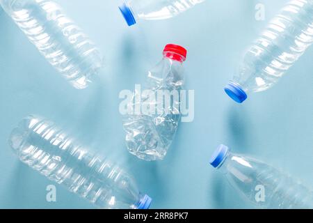 Wasserflaschen aus zerstoßenem Kunststoff mit blauen Kappen, die um die Wasserflasche aus zerstoßenem Kunststoff mit rotem Verschluss auf blauem Hintergrund stehen Stockfoto