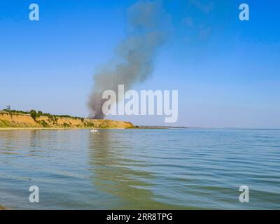 Rauch aus dem Feuer steigt in den Himmel über dem Asowschen Meer. Feuer an der Küste. Stockfoto