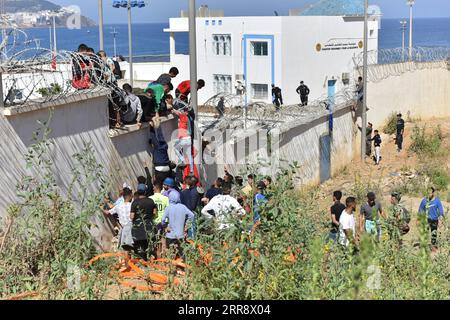 210519 -- FNIDEQ, 19. Mai 2021 -- Immigranten klettern über den Grenzzaun in die spanische Enklave Ceuta in Fnideq, Marokko, 18. Mai 2021. Die spanische Enklave Ceuta muss mit einem Zustrom von Einwanderern fertig werden, nachdem schätzungsweise 6.000 Menschen von Marokko aus in das Gebiet eingedrungen sind, so die Delegation der Zentralregierung in der Stadt. MAROKKO-FNIDEQ-SPANIEN-IMMIGRANTEN Xinhua PUBLICATIONxNOTxINxCHN Stockfoto