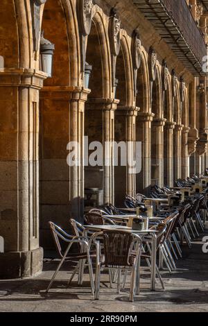 Leere Bartische und Korbsessel aus einem mittelalterlichen Restaurant neben den Säulen und Bögen des Hauptplatzes in Salamanca Stockfoto