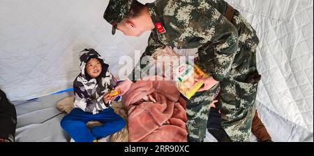 210522 -- PEKING, 22. Mai 2021 -- Foto mit dem Handy aufgenommen zeigt einen bewaffneten Polizisten, der sich in einem Zelt im Maduo County der tibetischen Autonomen Präfektur Golog, Provinz Qinghai im Nordwesten Chinas, um einen Jungen kümmert, 22. Mai 2021. Nach Erdbeben wurden bewaffnete Polizisten in die Provinzen Yunnan und Qinghai entsandt, um Rettungsarbeiten durchzuführen. Vier Erdbeben mit einer Stärke von mehr als 5,0 Magnitude schlugen das autonome Yangbi Yi County in der autonomen Präfektur Dali Bai Yunnan von 21 bis 23 Uhr Freitag, Beijing Time, ein. Das Zittern war in allen 12 Grafschaften und Städten der Präfektur zu spüren, wobei Yangbi am schlimmsten getroffen wurde Stockfoto