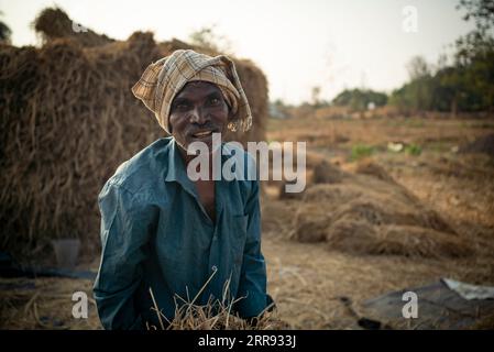 Karjat, Indien November 27 2022 Ein fleißiger, müder indischer Bauer, der auf einer Reisfarm und trockenem Gras steht, ist im Hintergrund gestapelt. Stockfoto