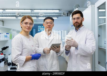 Porträt eines jungen interrassischen Teams aus Wissenschaftlern und Chemikern. Ein Mann und eine Frau stehen in einem Labor, arbeiten an einem Tablet und erforschen Kosmetik. Sie lächeln die Kamera an. Stockfoto