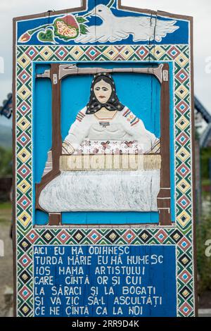 Ein hell bemaltes, geschnitztes Holzkreuz markiert das Grab eines Webers auf dem berühmten Frohen Friedhof im Dorf Săpânța, Maramureş, Rumänien Stockfoto