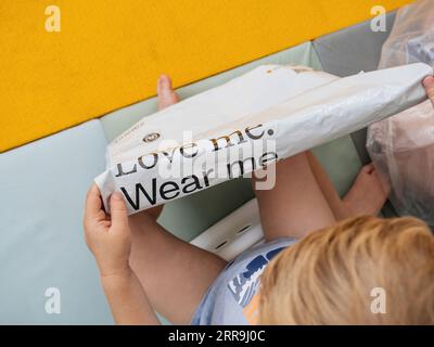 Hamburg, Deutschland - 24. Juli 2023: Kleinkind betrachtet die Bedeutung einer recycelbaren Plastiktüte mit dem Zalando-Logo und dem berührenden Slogan Love Me, Wear Me. Stockfoto