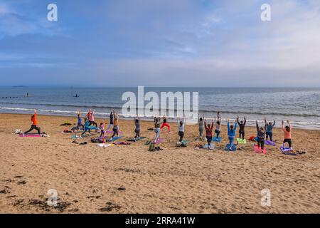 Gruppe von Frauen, die Yoga mit einer Lehrerin am Portobello Beach in Edinburgh, Schottland, Großbritannien, praktizieren. Stockfoto