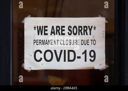 Papier, das in das Fenster eines Restaurants eingezogen wurde, mit der Aufschrift: „Es tut uns leid, es ist aufgrund von COVID-19 endgültig geschlossen“. Stockfoto