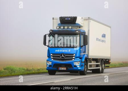 Der blaue Mercedes-Benz Lkw-Kühltransportanhänger liefert an einem nebligen Sommermorgen Güter auf der Autobahn 52. Salo, Finnland. August 25, 2023. Stockfoto