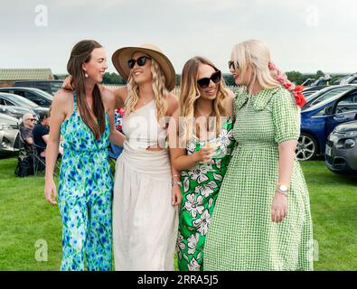 Eine Gruppe von vier Frauen lachte und lächelte und in farbenfrohen Kleidern gekleidet, genießt den Ladies Day bei den Rennen in Beverley, Großbritannien. Stockfoto