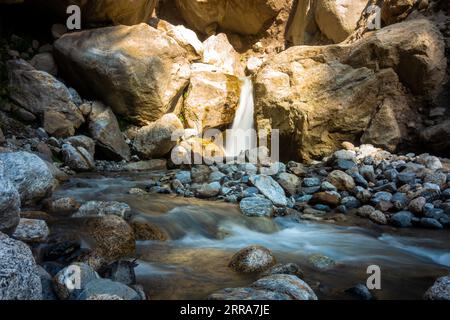 Malerischer Wasserfall im Himalaya inmitten massiver Felsen in Himachal Pradesh, Indien. Teil von Kinner Kailash Yatra, einer hinduistischen Pilgerreise. Langzeitbelichtung. Stockfoto