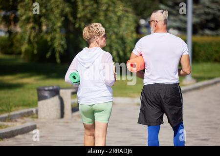 Rückansicht eines älteren Paares, eines Mannes und einer Frau in Sportbekleidung mit Fitness-Matte, Laufen, Training im Freien Stockfoto