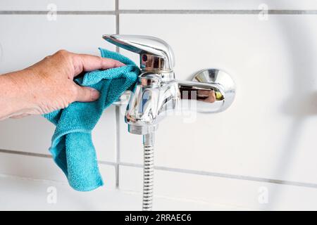 Reinigen eines Badewannenhahns mit einem blauen Mikrofasertuch, um Kalkflecken aus hartem Kalziumwasser zu entfernen, Kopierraum, ausgewählter Fokus, geringe Tiefe von Stockfoto