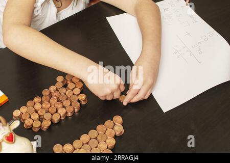 Ein kleines Mädchen, das ihr rettetes Kapital aus Münzen in ihrer Sparkasse organisiert und ihr Vermögen zählt Stockfoto