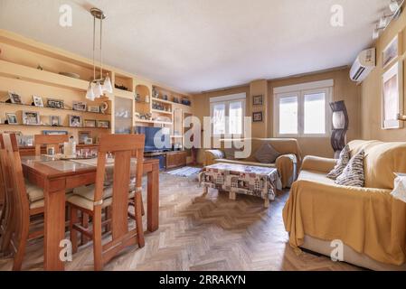 Ein Wohnzimmer voller Holzmöbel mit einem eingebauten Bücherschrank mit Nischen, Sofas mit wiederhergestellten Polstern und Eichenparkettböden Stockfoto