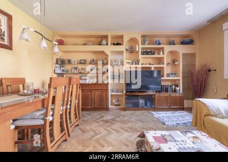 Ein Wohnzimmer mit Holzmöbeln, einem eingebauten Bücherregal mit Nischen, einem Esstisch mit passenden Stühlen, einem Flachbildfernseher und Eichenparkettböden Stockfoto