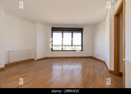 Ein leeres Wohnzimmer mit billigen Heizkörpern, einem großen dunkelgrauen Aluminiumfenster und Eichenholzböden Stockfoto