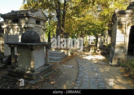 Ein Kopfsteinpflasterweg führt vorbei an alten Gräbern und Grabstätten auf dem historischen Pariser Friedhof Père Lachaise. Stockfoto