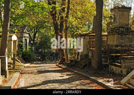 Eine Kopfsteinpflasterstraße führt vorbei an alten Gräbern und Grabstätten auf dem historischen Pariser Friedhof Père Lachaise. Stockfoto