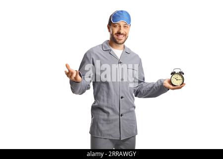 Junger Mann im Pyjama, der eine Uhr hält und vor der Kamera lächelt, isoliert auf weißem Hintergrund Stockfoto