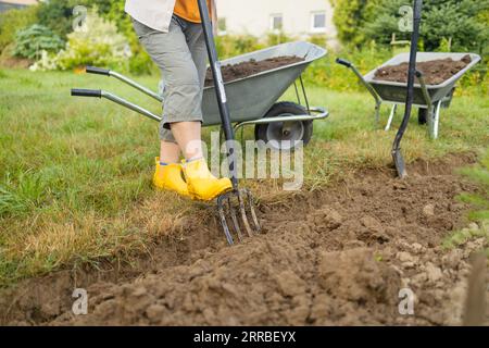 Landwirt, der mit Handwerkzeugen Land im Garten anbaut. Bodenlockerung. Gartenkonzept. Rechen und Spaten auf gelöstem Boden. Landwirtschaftliche Arbeiten Stockfoto